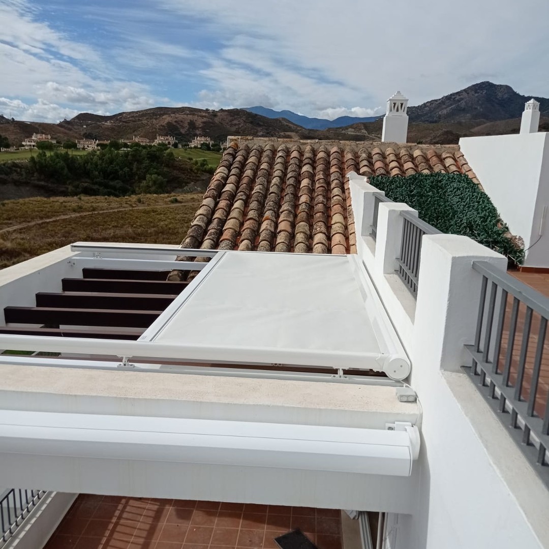 Toldo retráctil blanco instalado en una terraza residencial con vista a montañas y tejados tradicionales.