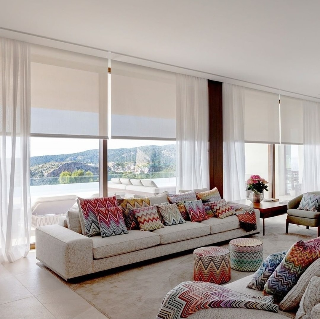 Elegante salón con amplios ventanales cubiertos por cortinas blancas semitransparentes que ofrecen vistas al paisaje exterior.