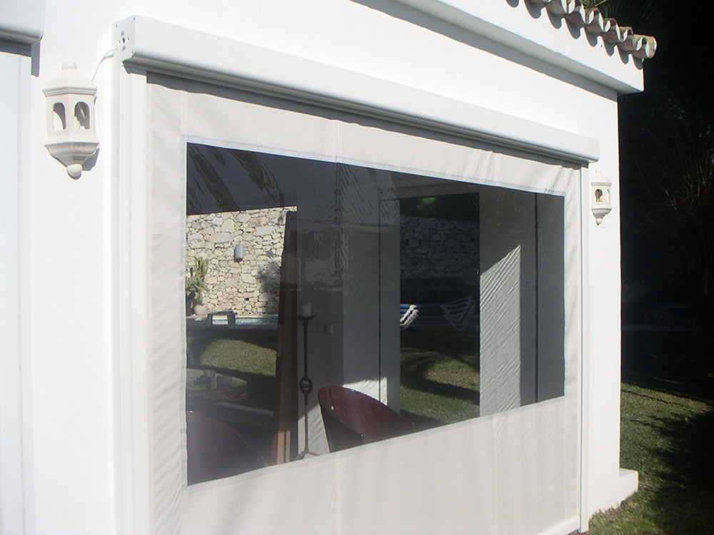 Persiana enrollable de malla blanca proporcionando sombra y privacidad a una terraza exterior.